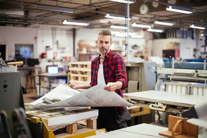 Man in red and blue plaid shirt looking at different types of large printing paper in local NYC print shop