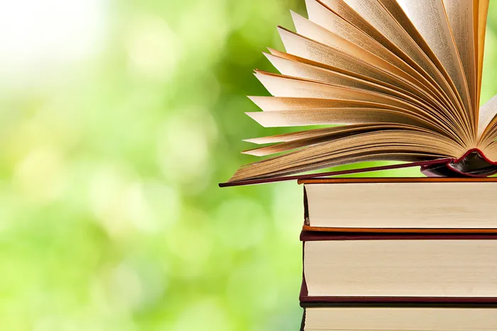 Four books stacked on top of each other with the top one open to show pages fanning