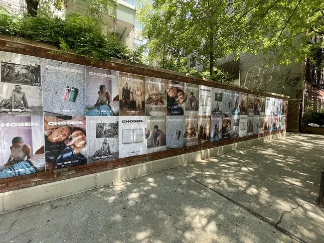 Wheat paste posters on a wall next to a sidewalk in NYC